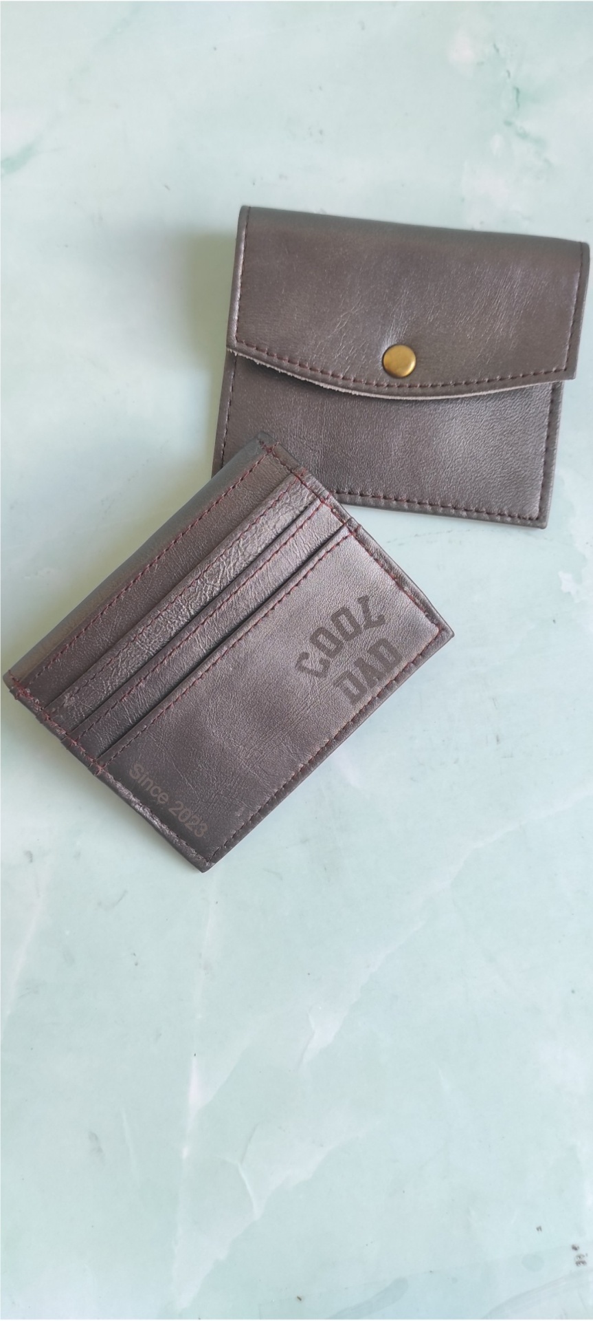 Carteira e porta-moedas castanhos escuros com textos COOL AID e SINCE 2023