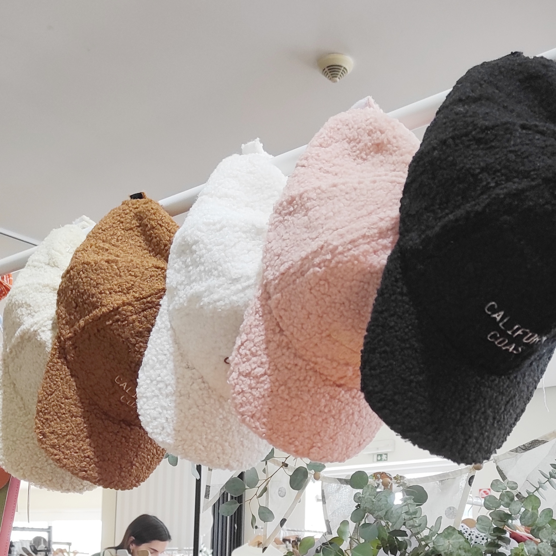 Cinco bonés peludos coloridos pendurados numa barra branca