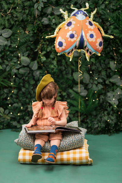 Criança a ler sentada em almofadas com balão de joaninha ao fundo