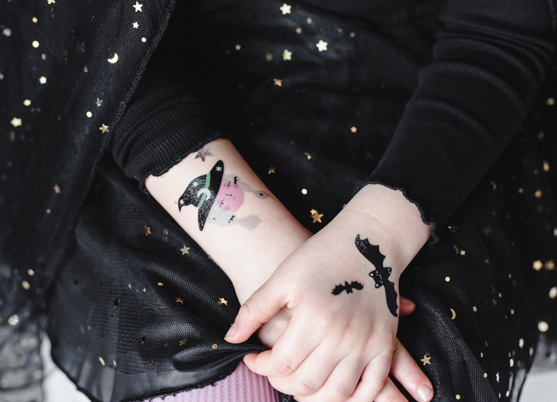 Tatuagens temporárias de bruxa e morcegos nas mãos de criança com roupa preta com estrelas