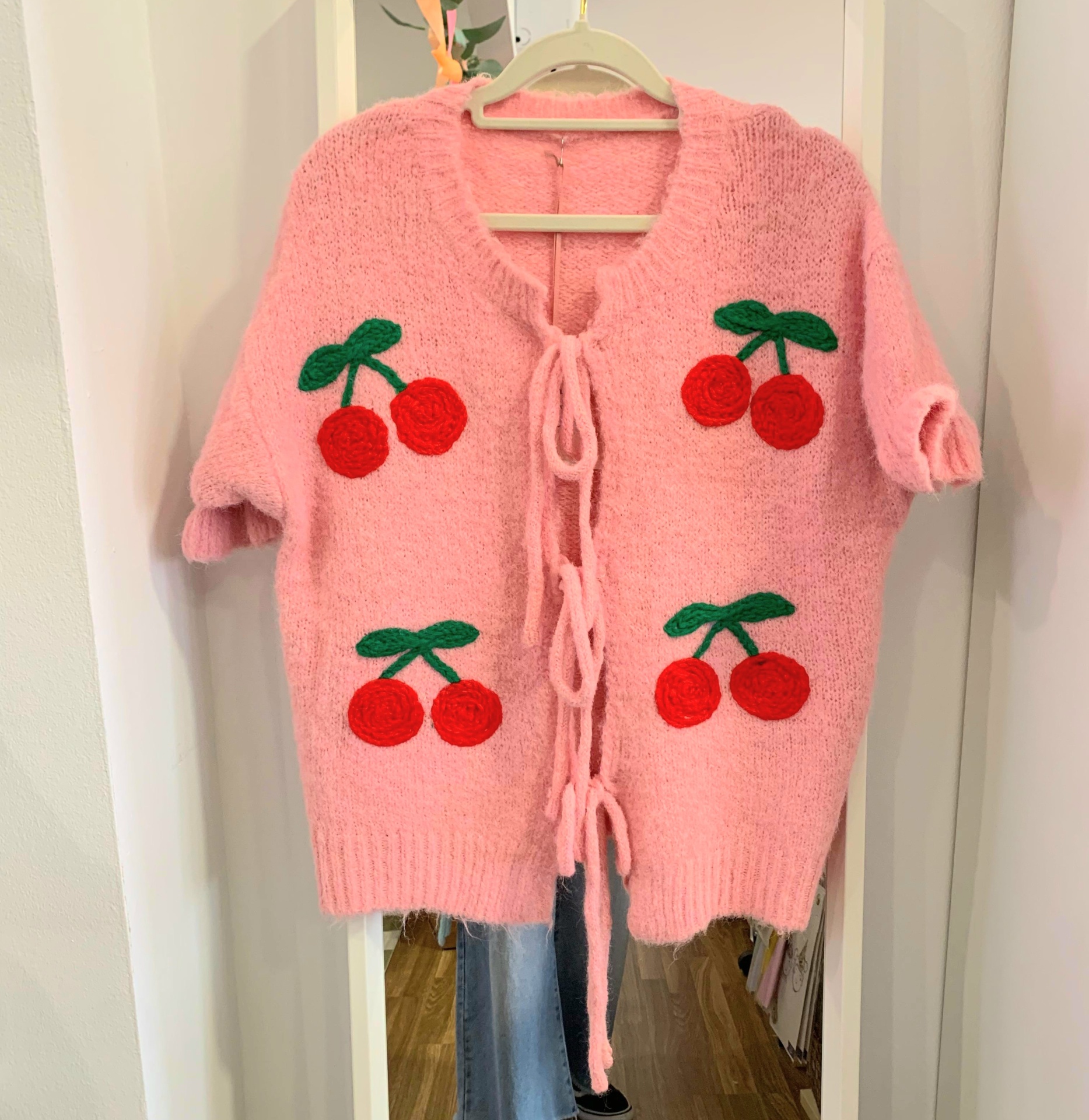 Casaco rosa de malha com cerejas vermelhas e folhas verdes pendurado num cabide.