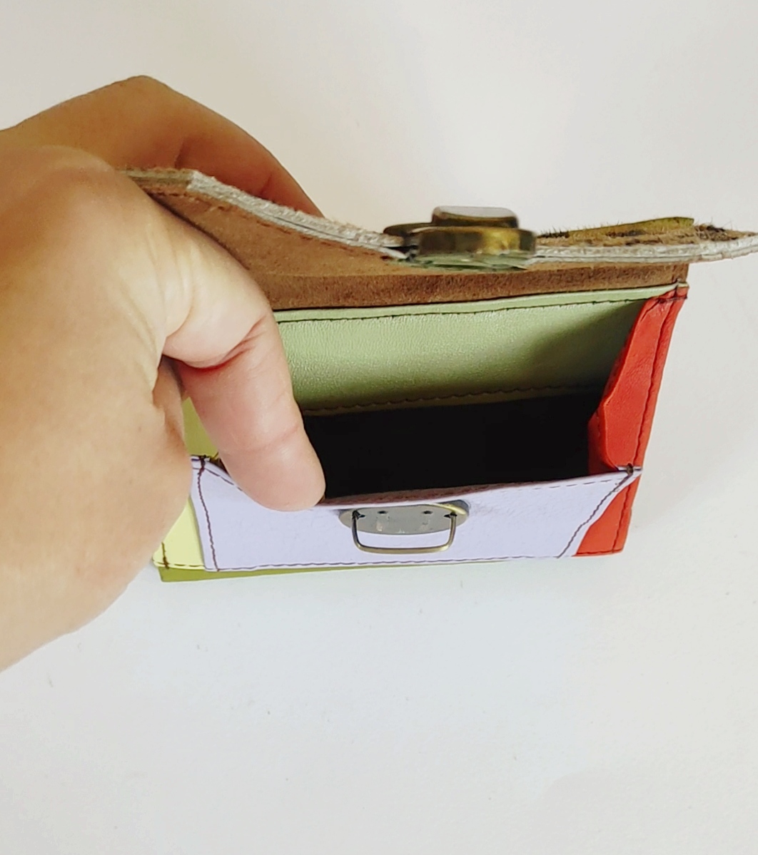 Carteira colorida aberta com botão metálico e mão a segurá-la