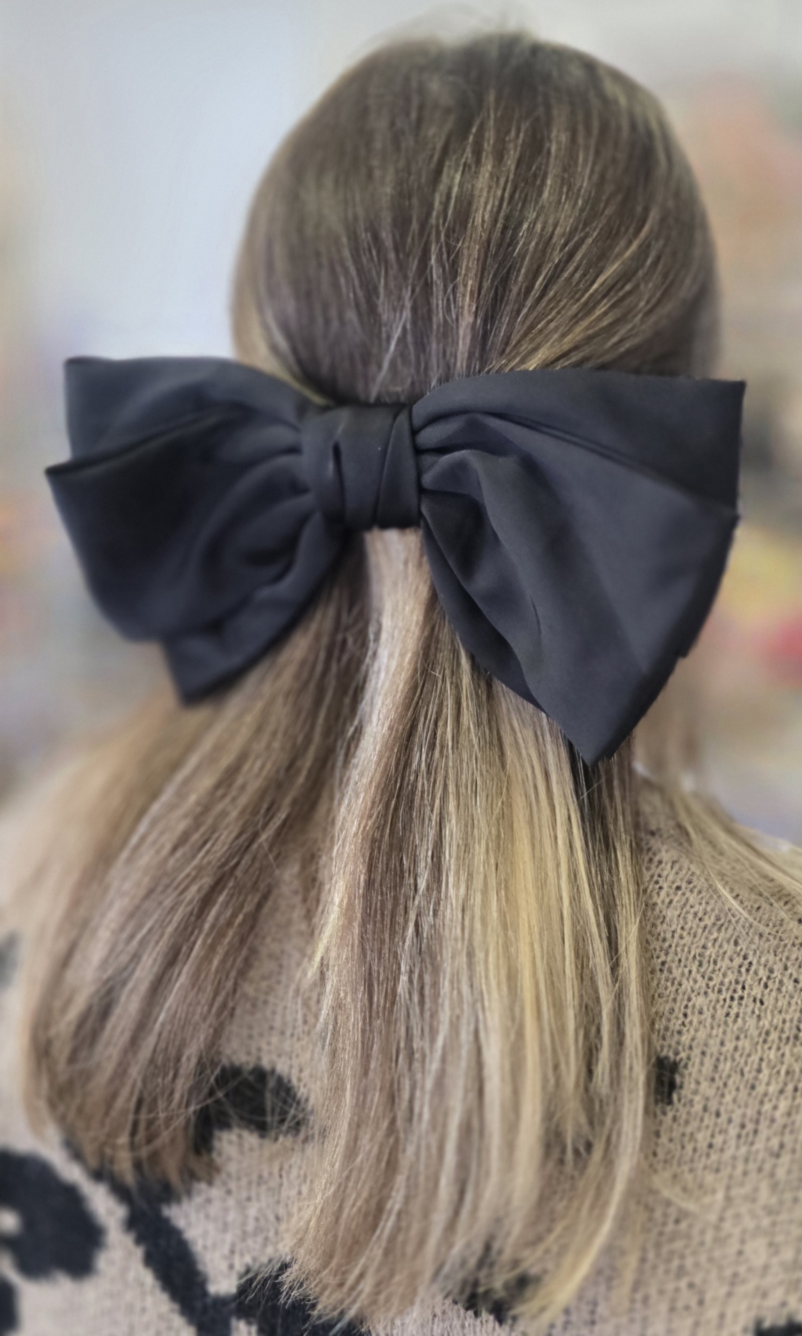 Laço preto de tecido no cabelo loiro de uma pessoa com camisola bege e padrão preto.