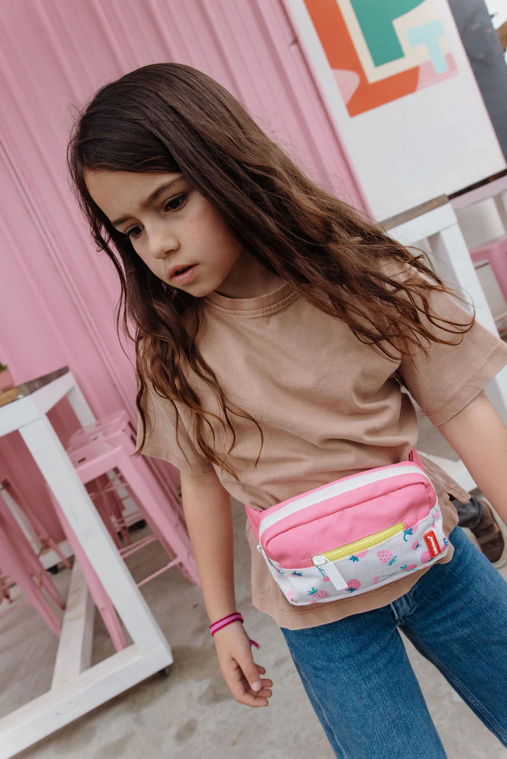 Menina com pochete rosa, camiseta bege e calças de ganga em ambiente interior