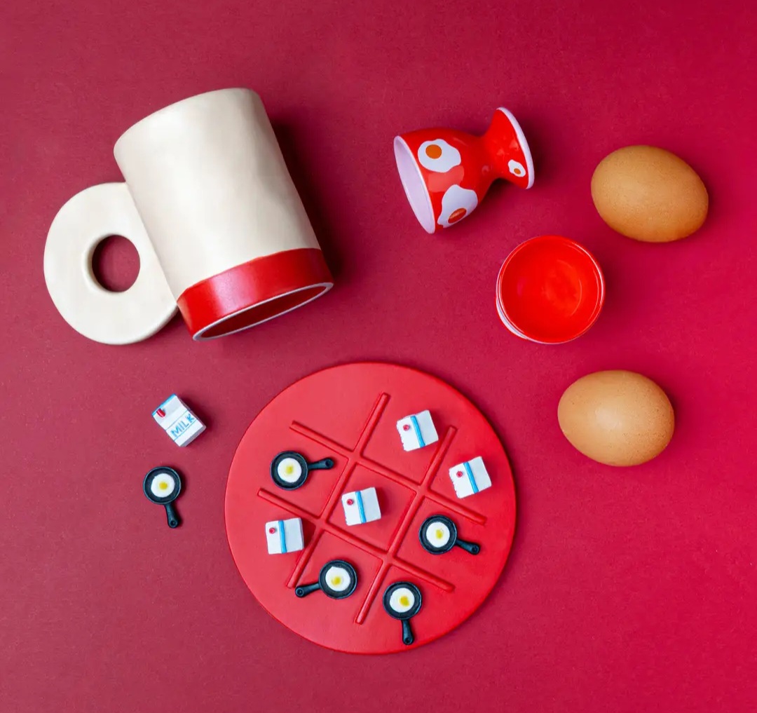 Jogo da velha com peças miniatura e utensílios de cozinha coloridos sobre fundo vermelho