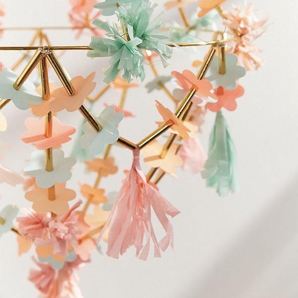 Decoração suspensa com flores e franjas de papel em cores pastéis sobre estrutura metálica dourada