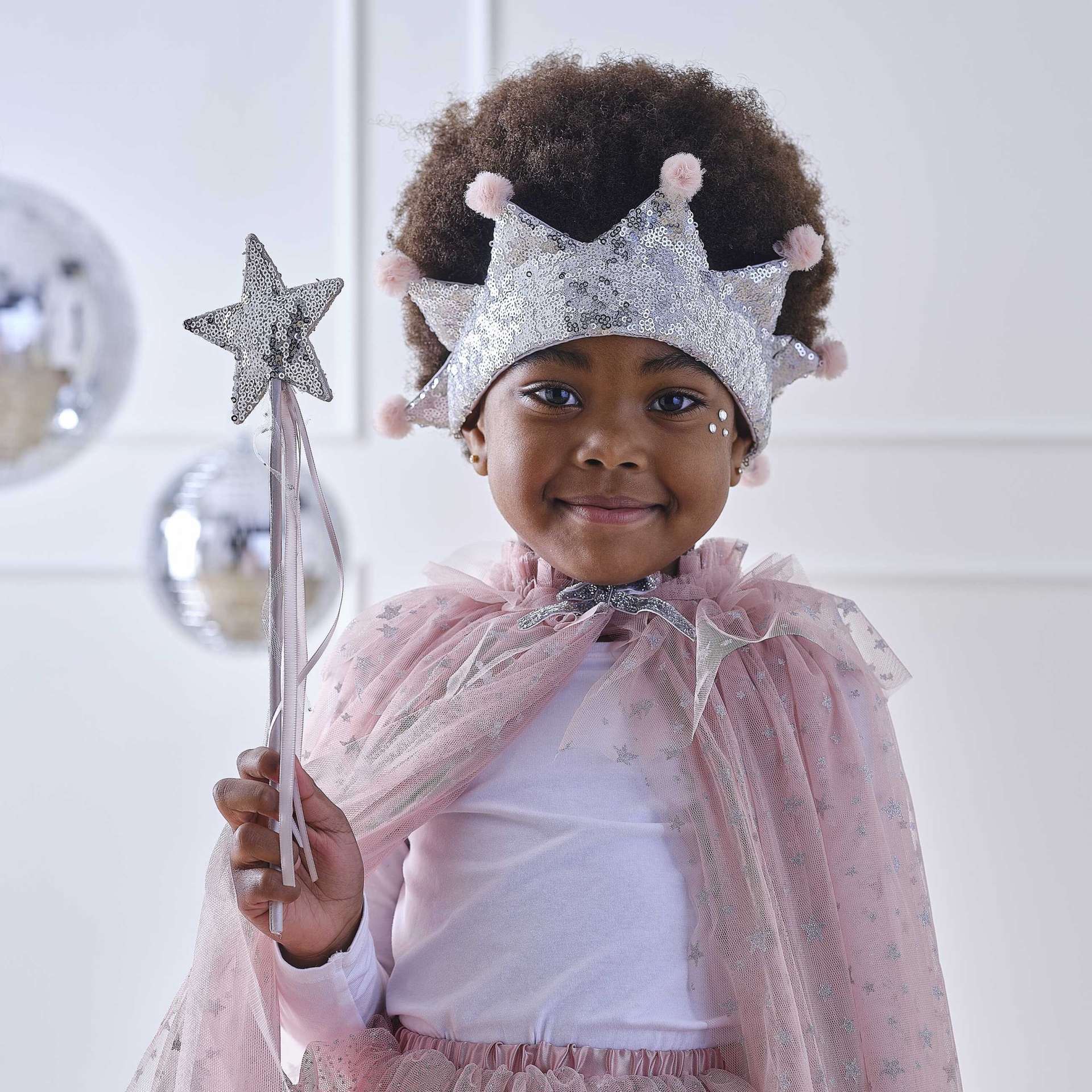 Criança com coroa prateada e capa cor-de-rosa segurando varinha de estrela