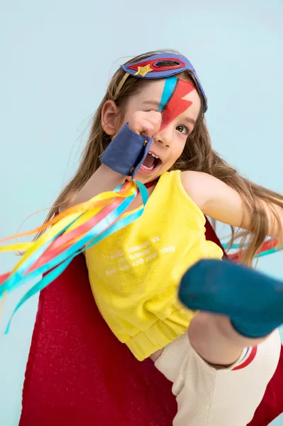 Criança com traje de super-herói colorido e máscara no fundo azul claro