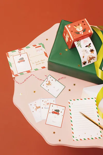 Papelaria e embrulhos de Natal com cartões, etiquetas, envelopes e fita adesiva em fundo laranja