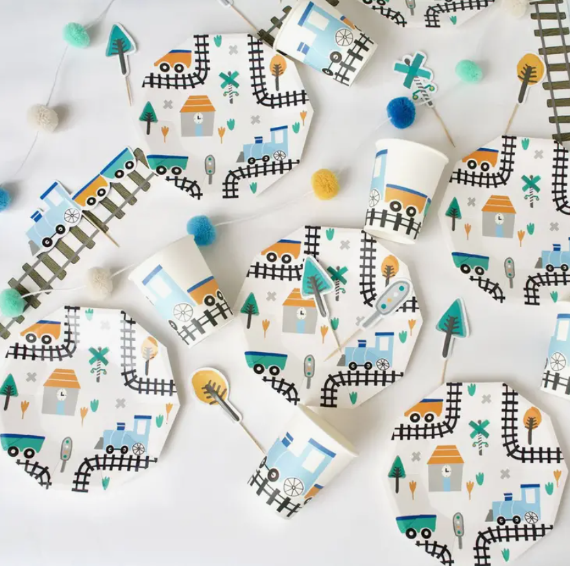 Pratos e copos descartáveis com padrão de trem e pompons de feltro coloridos para festa infantil