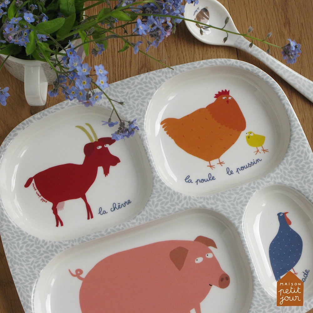 Pratos de cerâmica com desenhos de animais da quinta e texto em francês sobre mesa de madeira com flores azuis