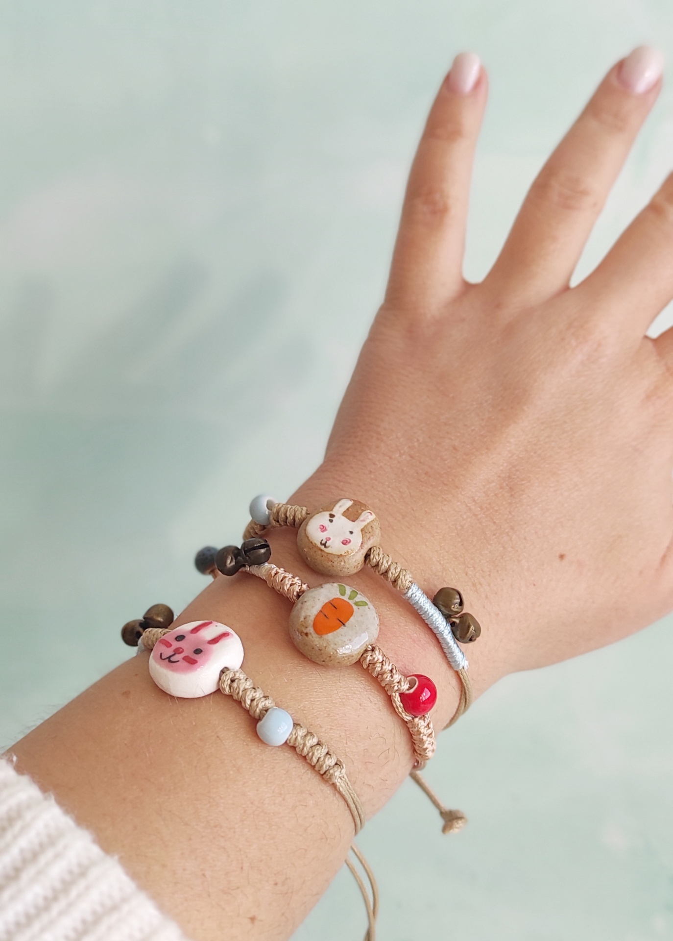 Pulseiras trançadas com contas de cerâmica de coelho e cenoura no pulso de uma pessoa