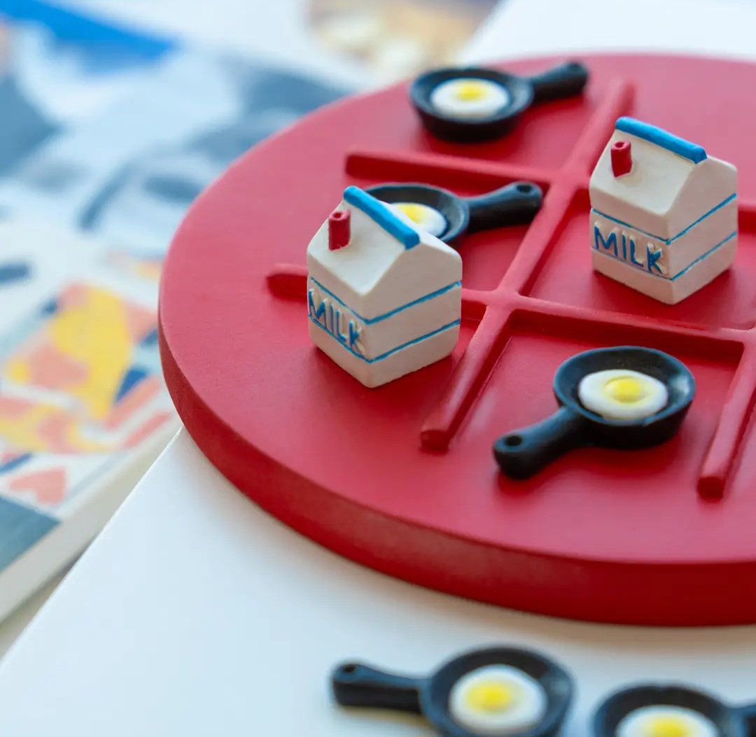Jogo da velha com peças de leite e ovos em frigideiras sobre tabuleiro vermelho