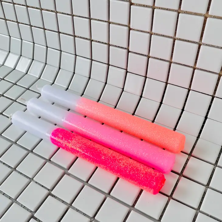 Três canetas de glitter rosa e laranja sobre azulejos brancos com linhas pretas