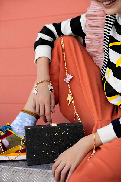 Pessoa com roupa colorida segurando uma mala preta com corrente dourada