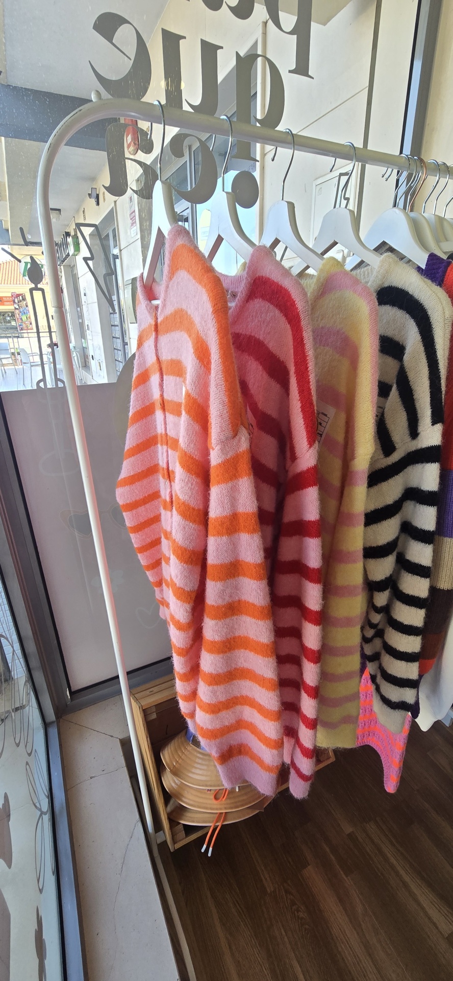 Casacos de malha com riscas coloridas pendurados em cabides numa loja