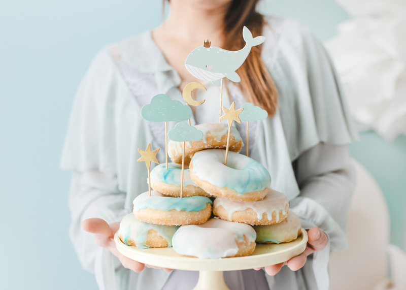Donuts decorados com glacê branco e azul pastel numa base com decorações de estrelas, nuvens, lua e baleia