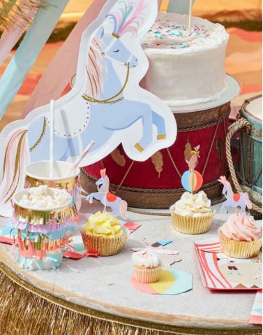 Mesa com bolos, cupcakes decorados com cavalos de carrossel e tambor vermelho ao fundo