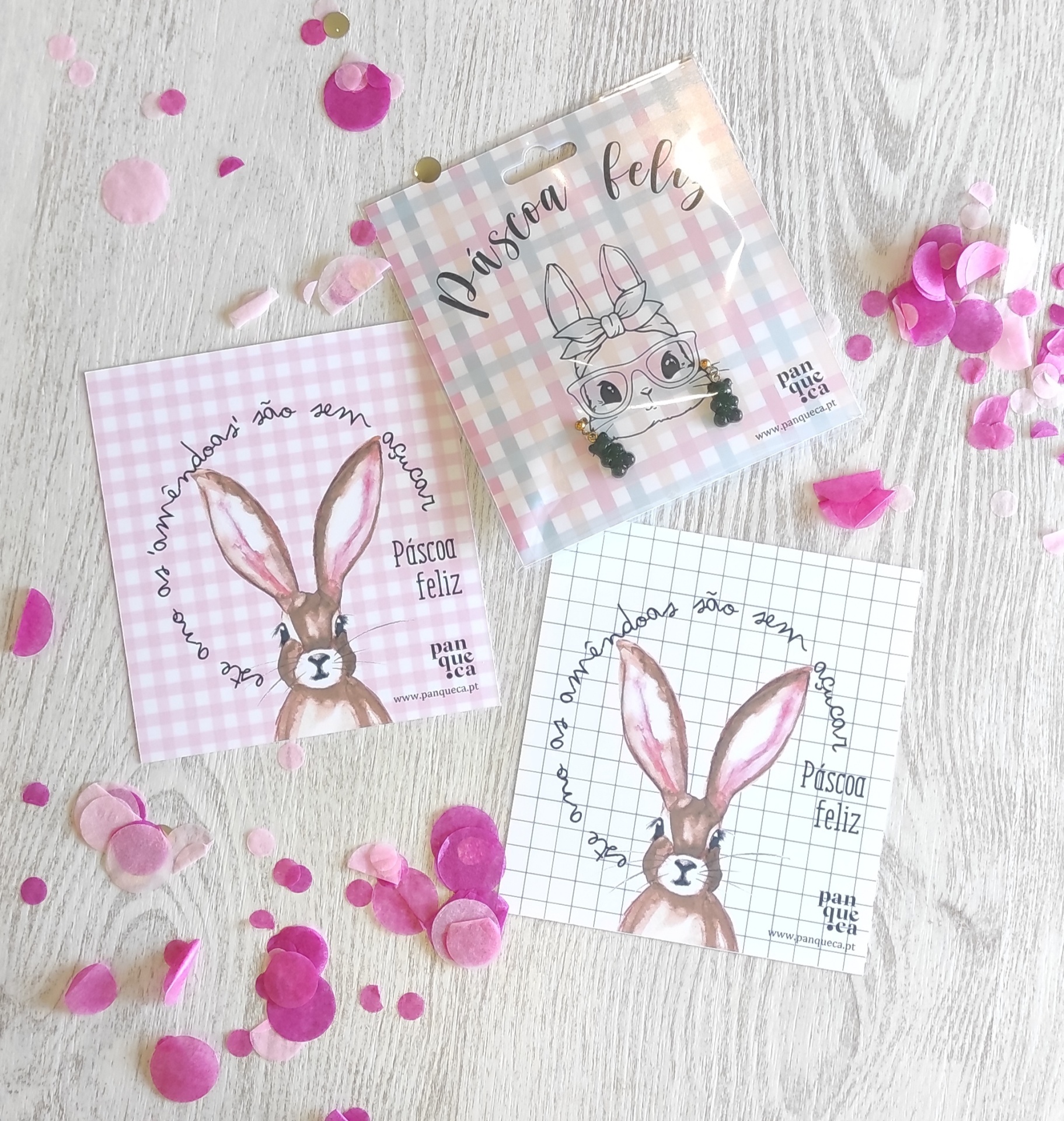 Guardanapos decorativos de Páscoa com desenhos de coelho e texto em português sobre fundo xadrez e confetes rosa à volta.