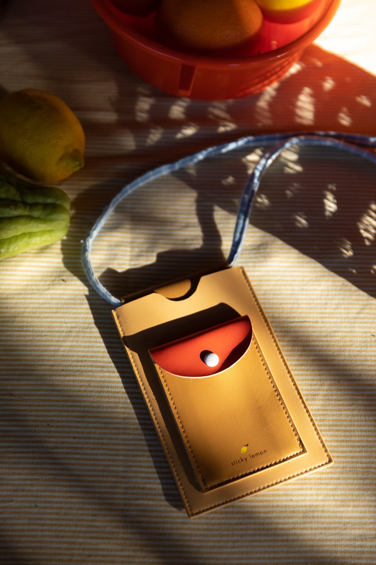 Carteira pequena castanha e vermelha com cordão azul com frutas e tecido ao fundo