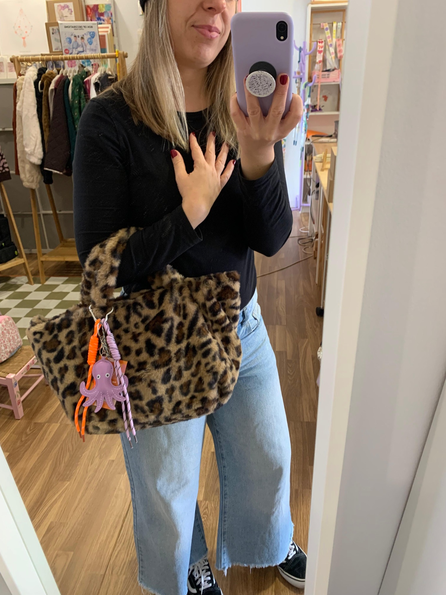 Mulher com mala de padrão leopardo e chaveiro de polvo tirando selfie no espelho numa loja