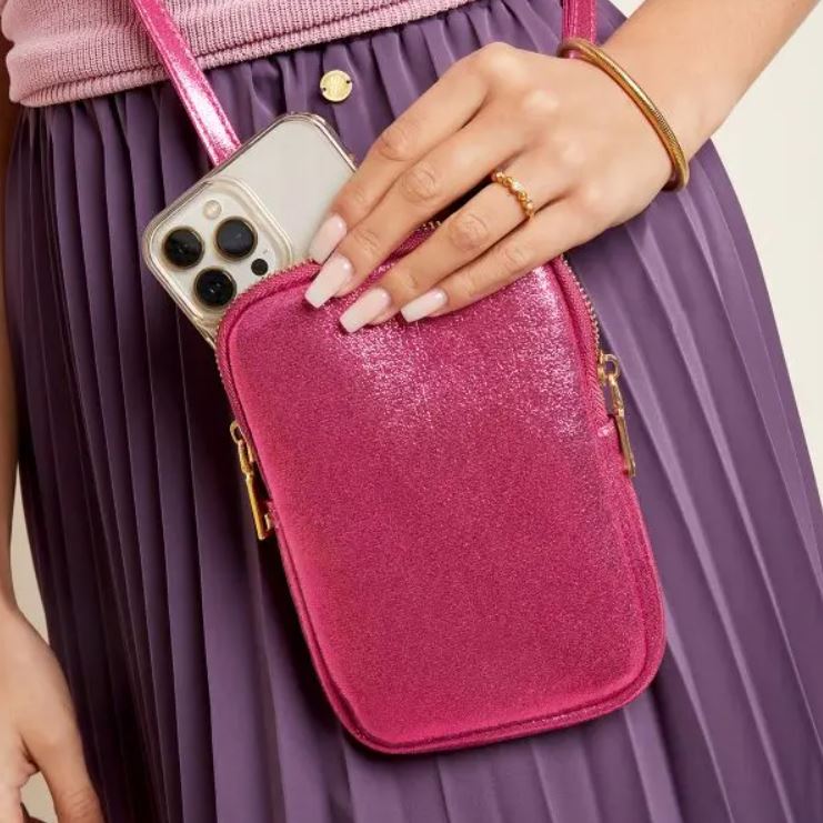 Bolsa pequena rosa brilhante com telemóvel prateado num fundo de saia roxa plissada
