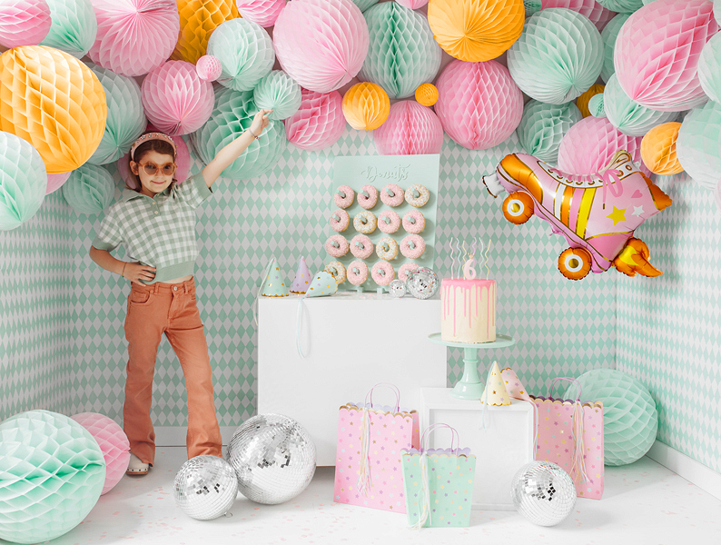 Decoração de festa de aniversário com balões pastel, bola prateada, bolo cor-de-rosa e presentes coloridos.