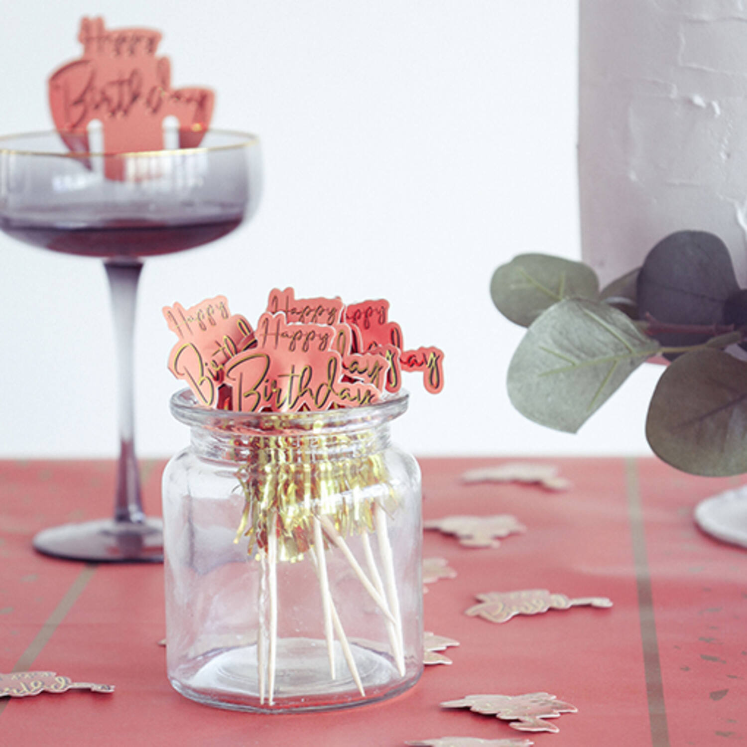 Palitos decorativos Happy Birthday em frasco de vidro sobre mesa vermelha