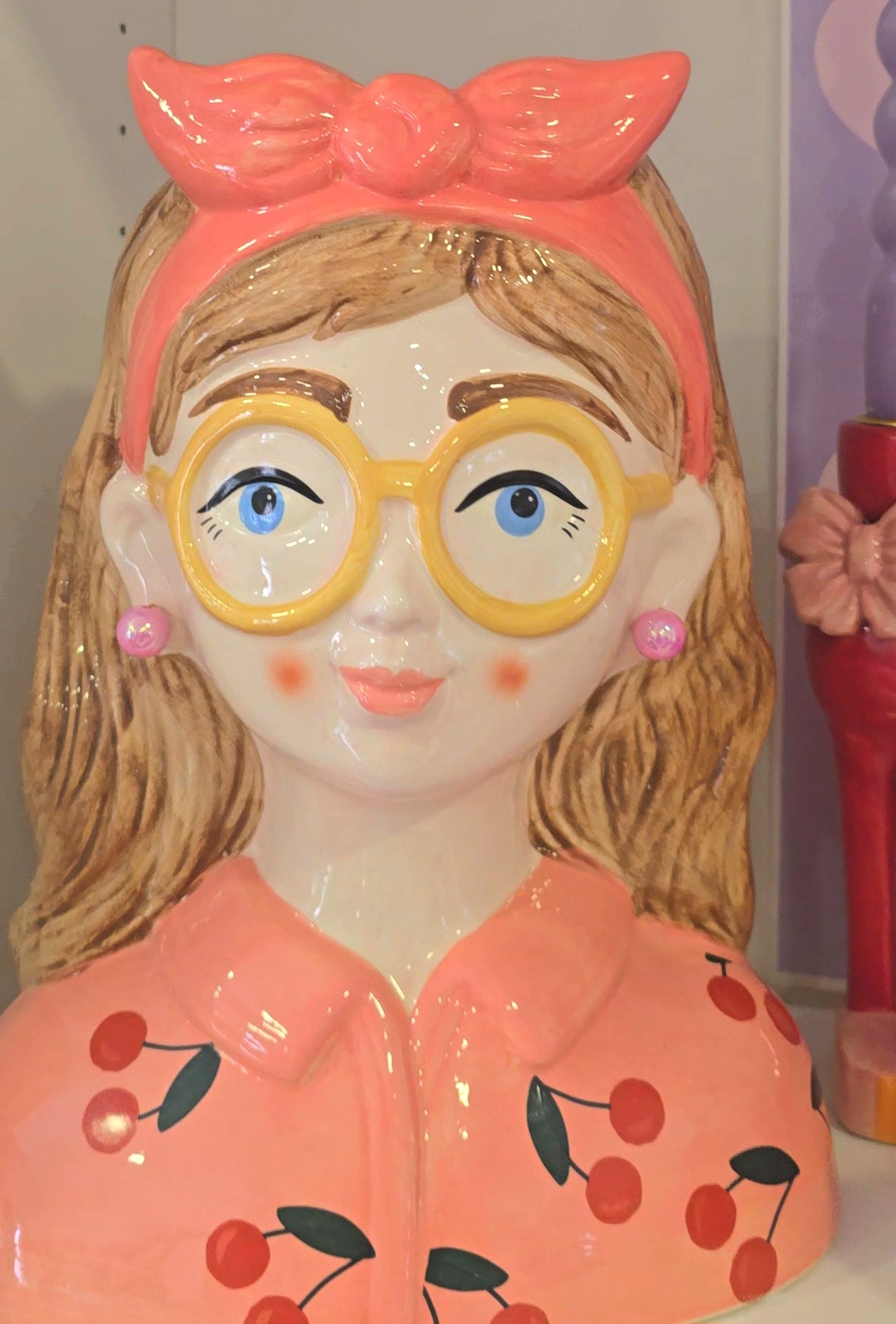 Estátua decorativa mulher com óculos amarelos e camisa rosa com padrão de cerejas