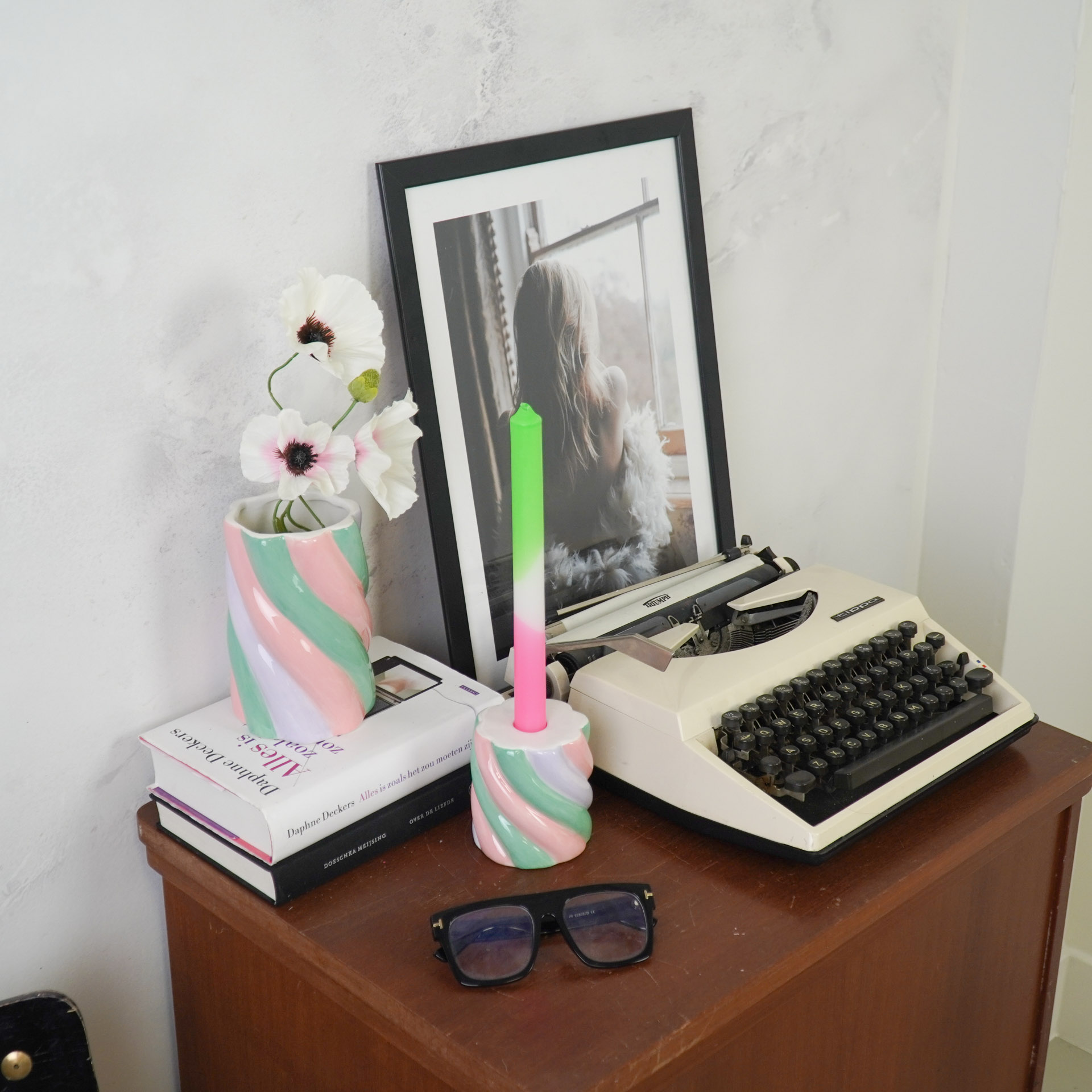 Vaso e castiçal com padrão colorido em espiral numa mesa de madeira com máquina de escrever, livros e óculos