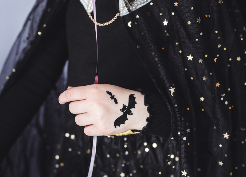 Mão infantil com tatuagem temporária de morcegos e capa preta com estrelas