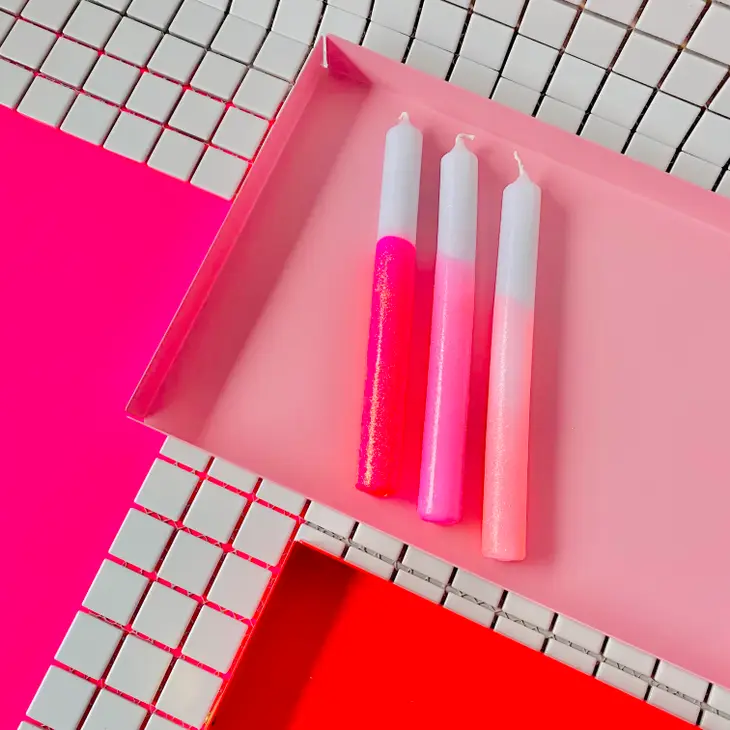 Três velas rosas e brancas em gradiente numa bandeja rosa sobre superfície com azulejos brancos e linhas pretas