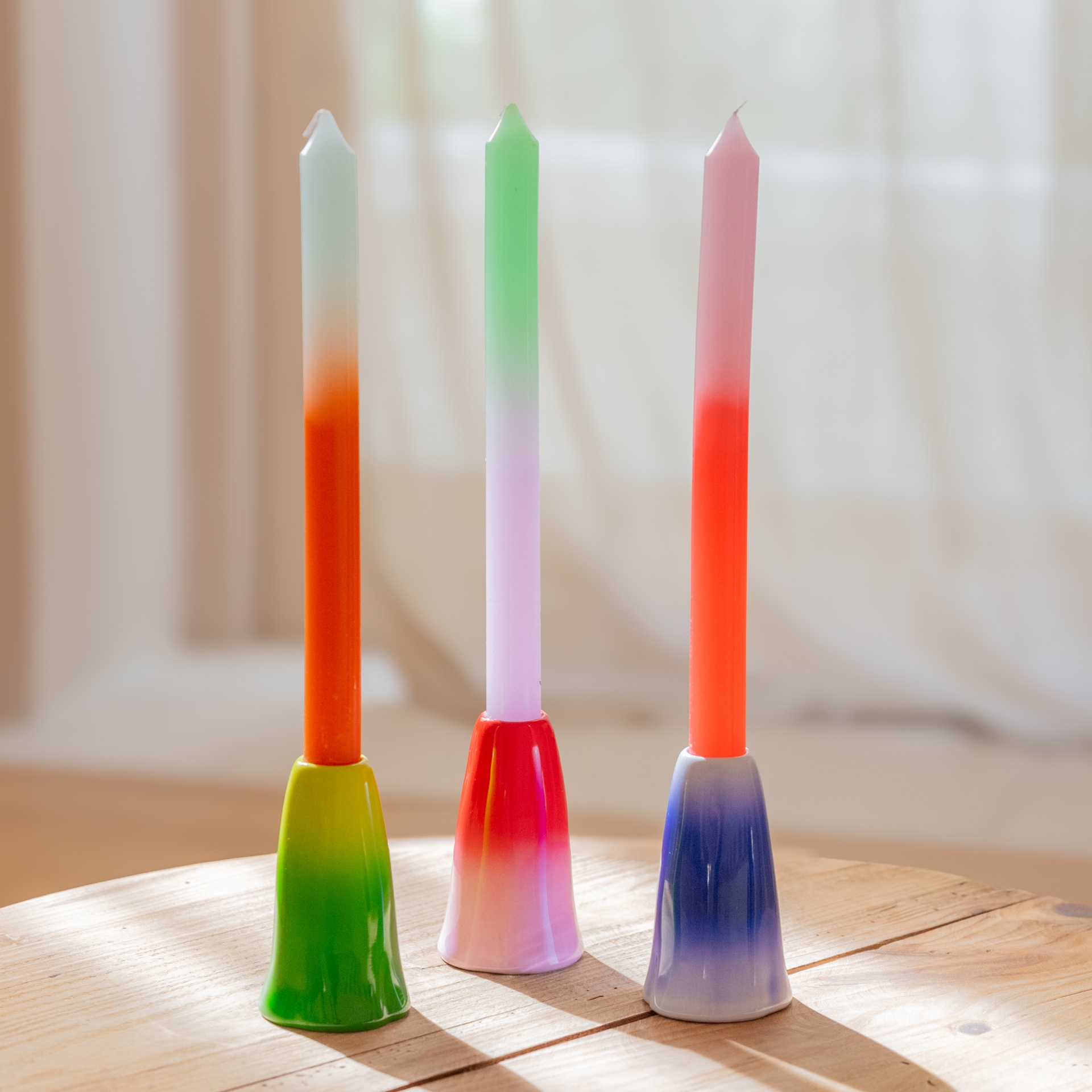 Três velas coloridas em castiçais de cerâmica sobre mesa de madeira