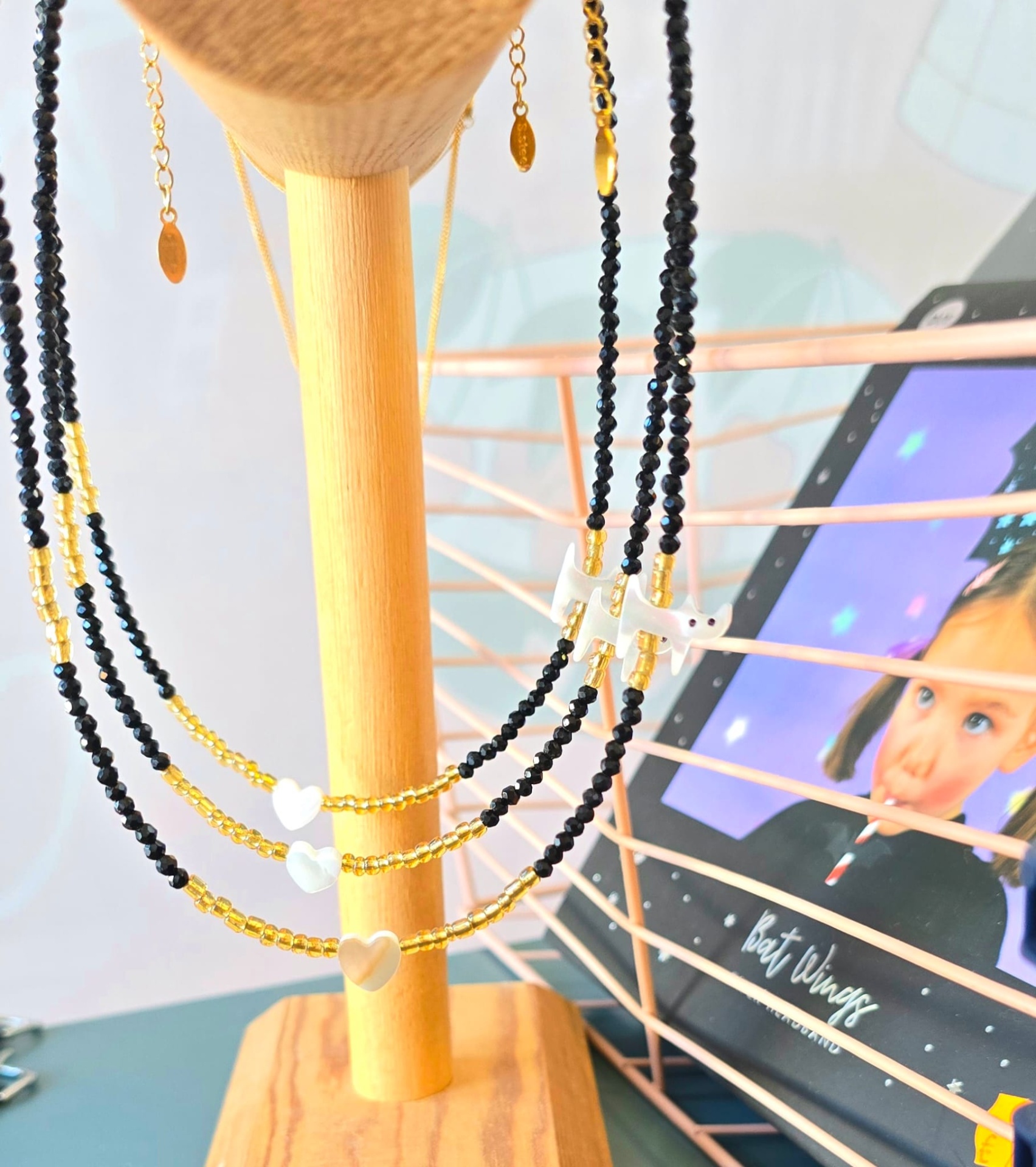 Colares em contas pretas e douradas com pendentes em forma de coração pendurados em suporte de madeira