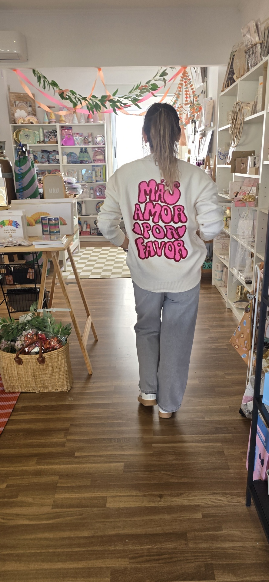 Camisola branca com texto rosa nas costas, calças cinza e sapatilhas em loja decorada