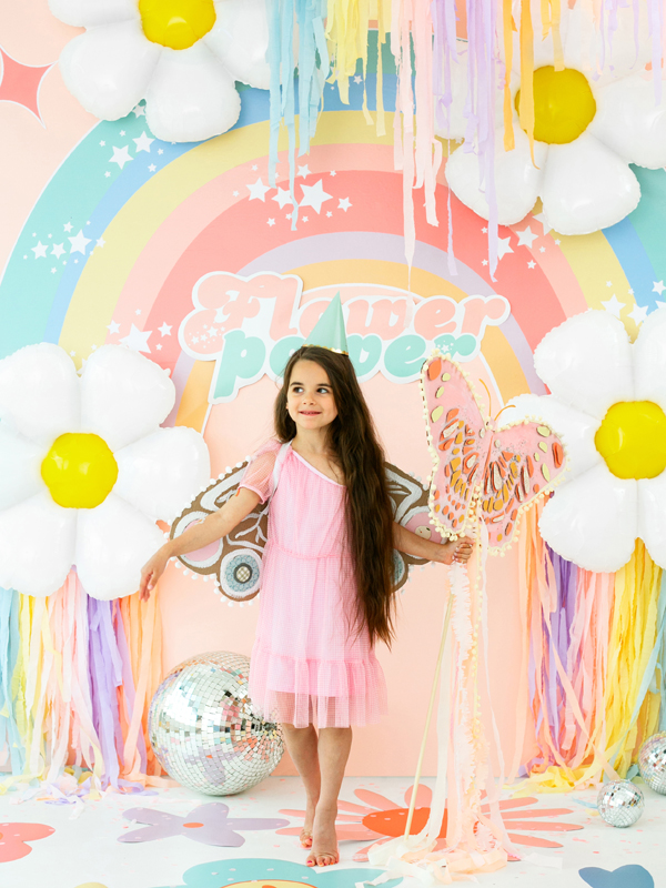 Menina de vestido rosa em festa decorada com flores, arco-íris e balões coloridos