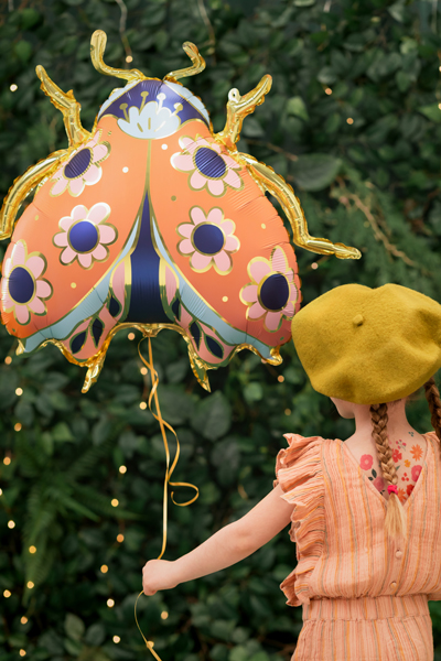 Balão joaninha floral metálico laranja e dourado com criança de vestido laranja e boina verde