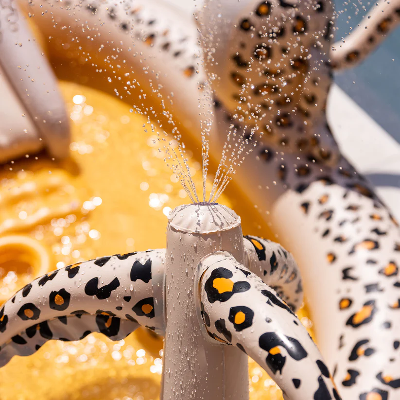 Fonte cerâmica branca com manchas de leopardo e jatos de água num fundo amarelo