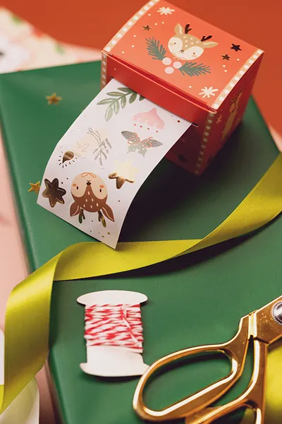 Caixa vermelha com fita adesiva natalícia e material de embrulho verde e amarelo