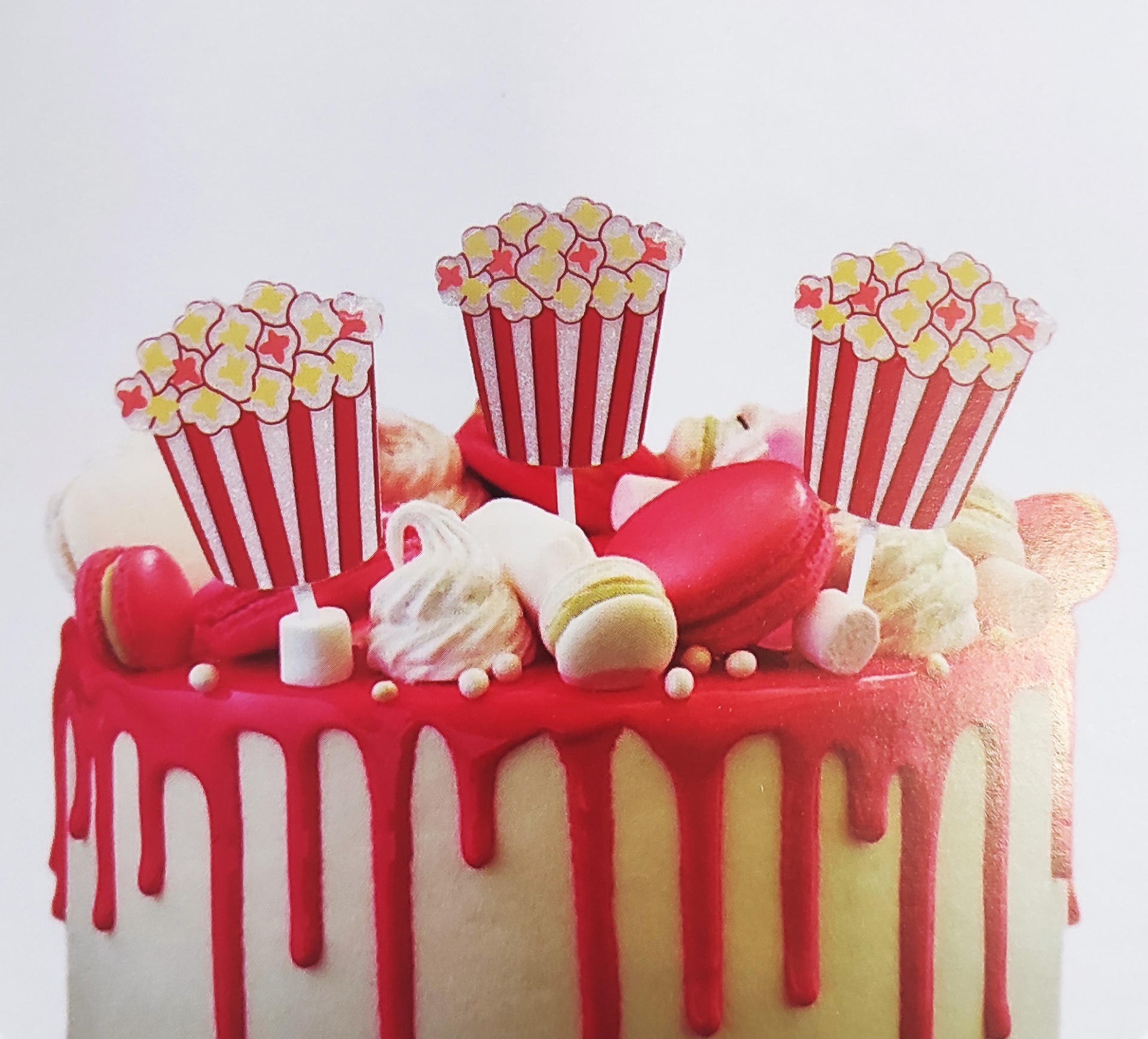 Bolo decorado com cobertura branca e calda vermelha e toppers de pipocas