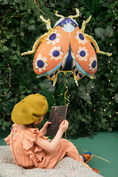 Balão metalizado em forma de joaninha com padrão floral e criança a segurá-lo