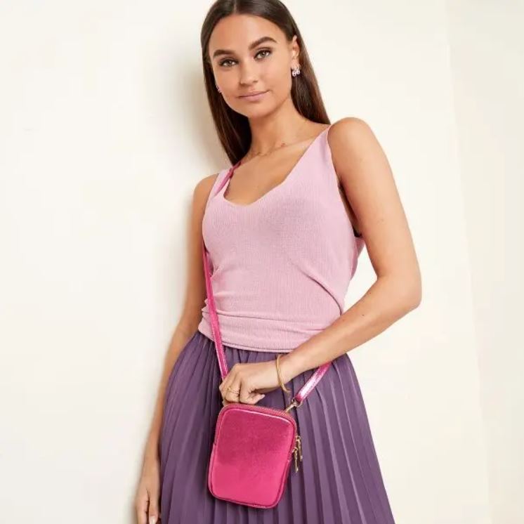 Mulher vestindo regata rosa, saia roxa plissada e bolsa rosa pequena