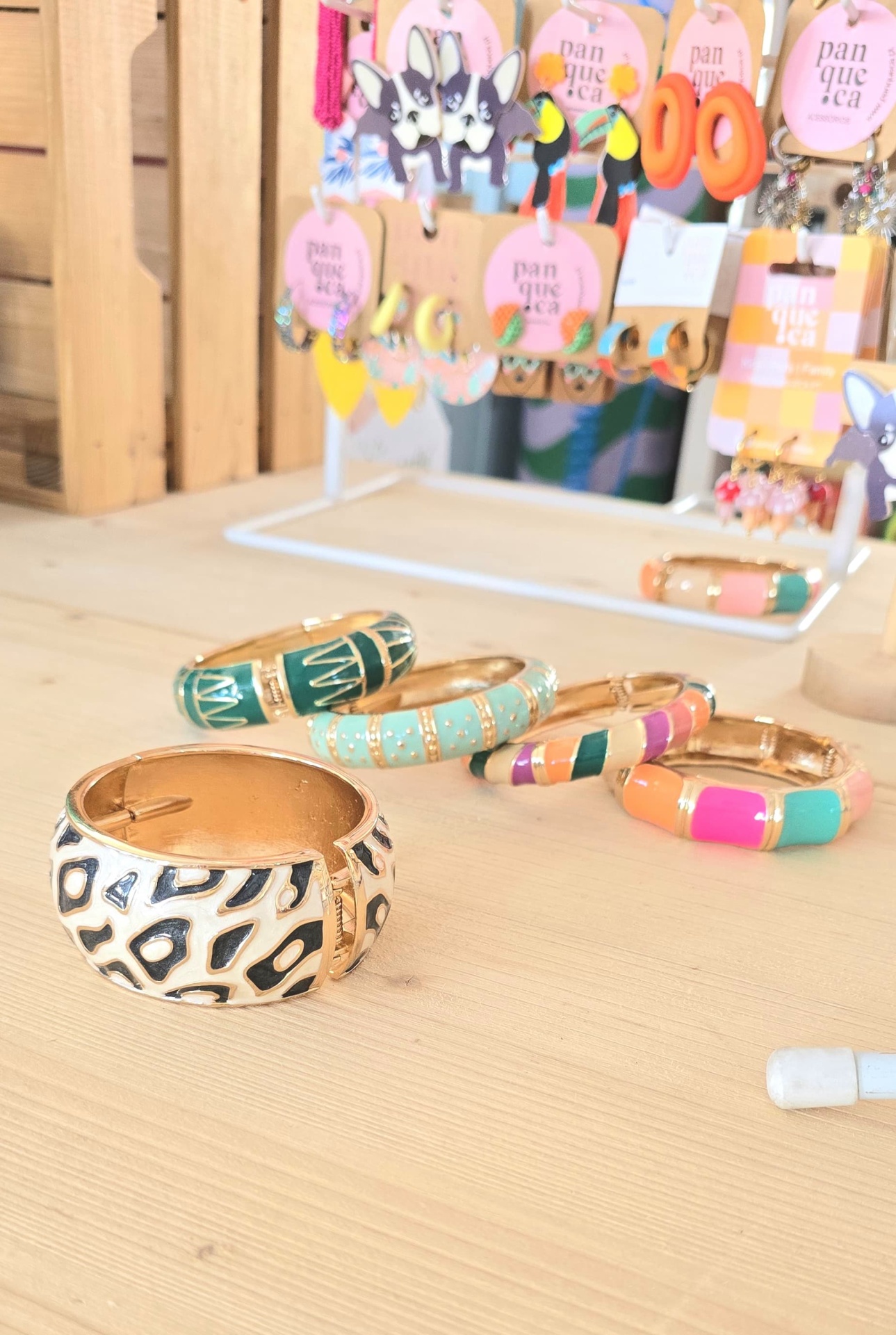 Braceletes coloridos em metal dourado com fundo de brincos em exposição