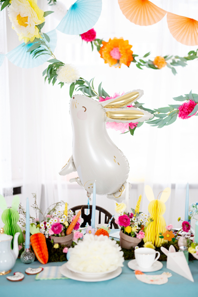 Balão de coelho branco com orelhas douradas numa mesa colorida decorada para festa