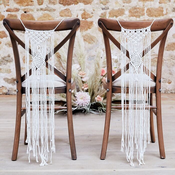 Duas cadeiras de madeira com pendentes de macramé branco pendurados nos encostos