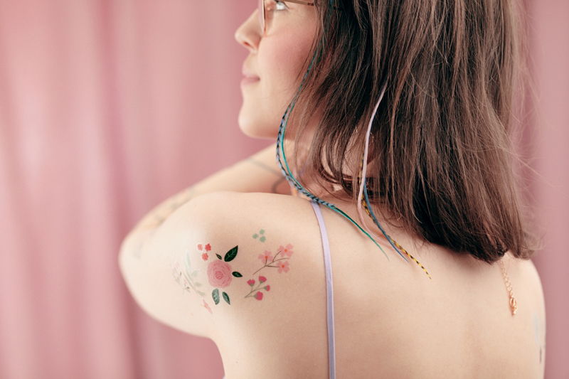 Mulher com tatuagem floral no ombro e cabelo com fios coloridos