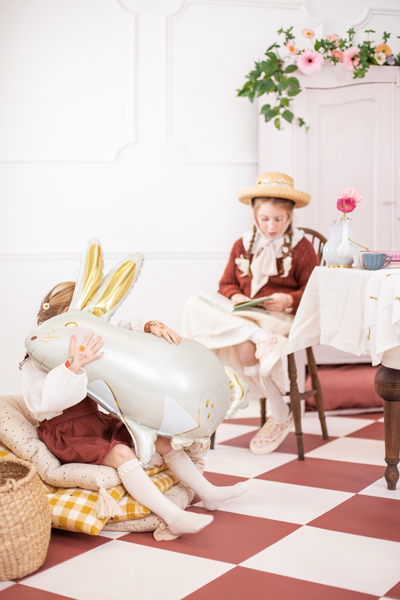 Crianças com balão de coelho em sala decorada com flores e mesa com toalha