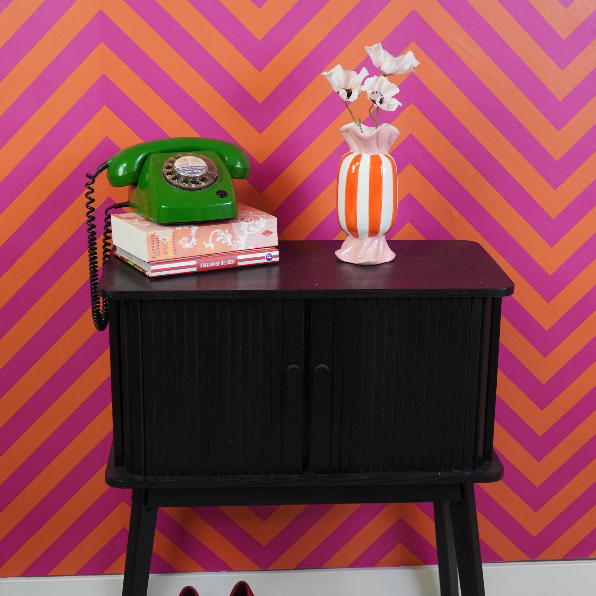 Telefone verde retro e vaso cerâmico com flores em mesa preta contra parede laranja e rosa