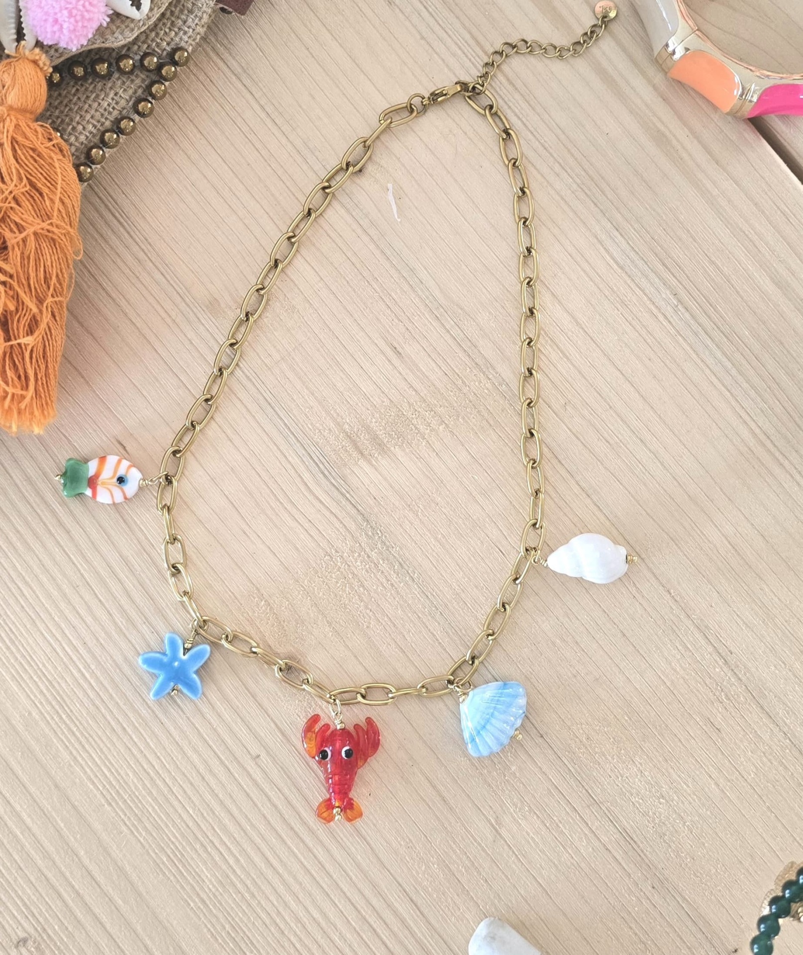Colar dourado com pendentes de estrela do mar, lagosta e conchas sobre mesa clara