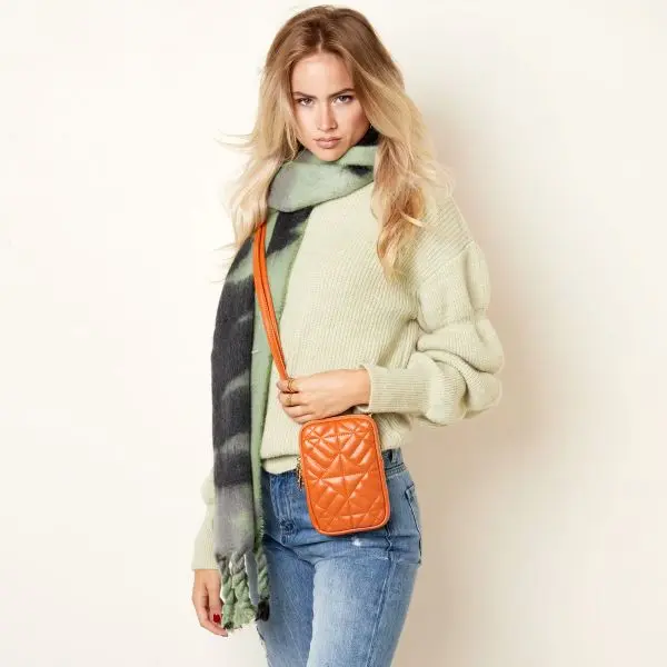 Mulher com camisola bege, jeans, cachecol verde e bolsa laranja acolchoada